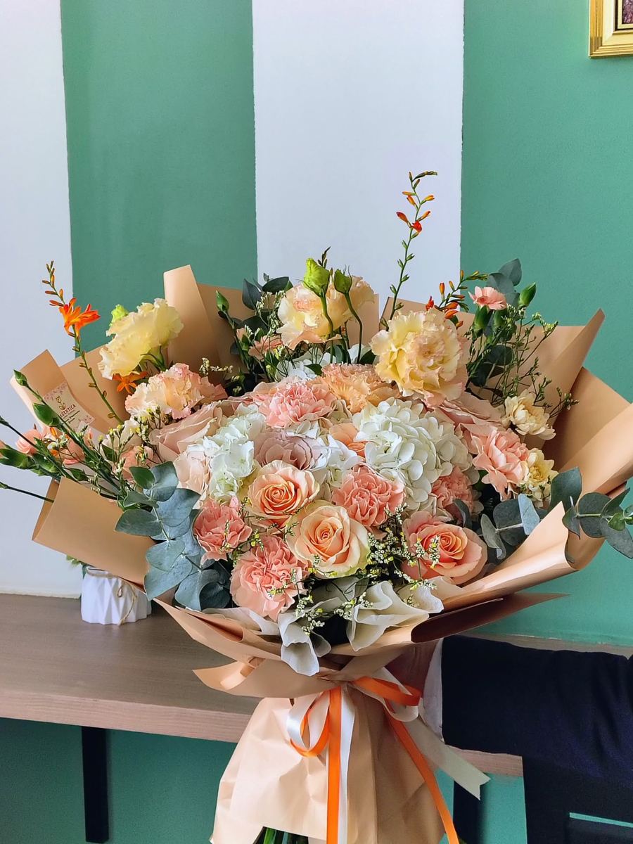 Ramo otoñal de rosas durazno y rosas, flores blancas y eucalipto, envuelto en papel kraft con listón naranja