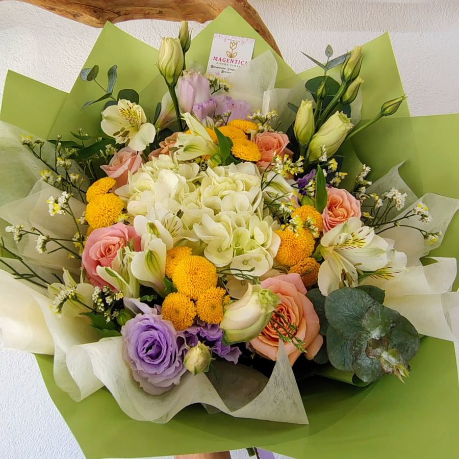 Ramo en papel verde con hortensia crema, rosas durazno, alstroemerias, lisianthus lila, botón amarillo y eucalipto